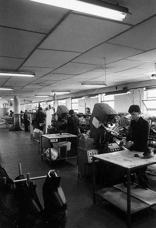 Mustavalkoinen, vanha kuva, jossa Giascon tehtaan työntekijät valmistavat kenkiä.